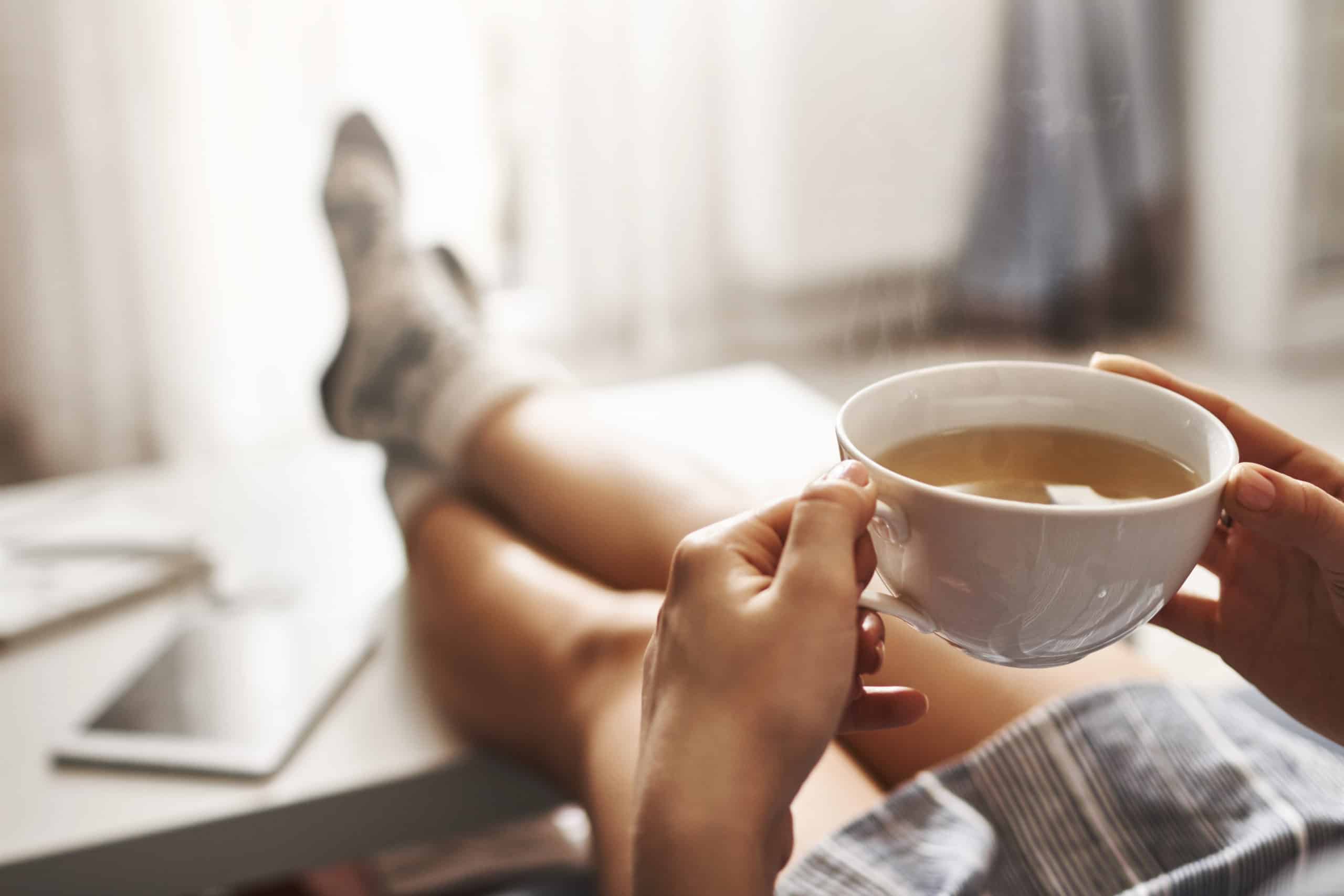 cup-tea-chill-woman-lying-couch-holding-legs-coffee-table-drinking-hot-coffee-enjoying-morning-being-dreamy-relaxed-mood-girl-oversized-shirt-takes-break-home-1-scaled